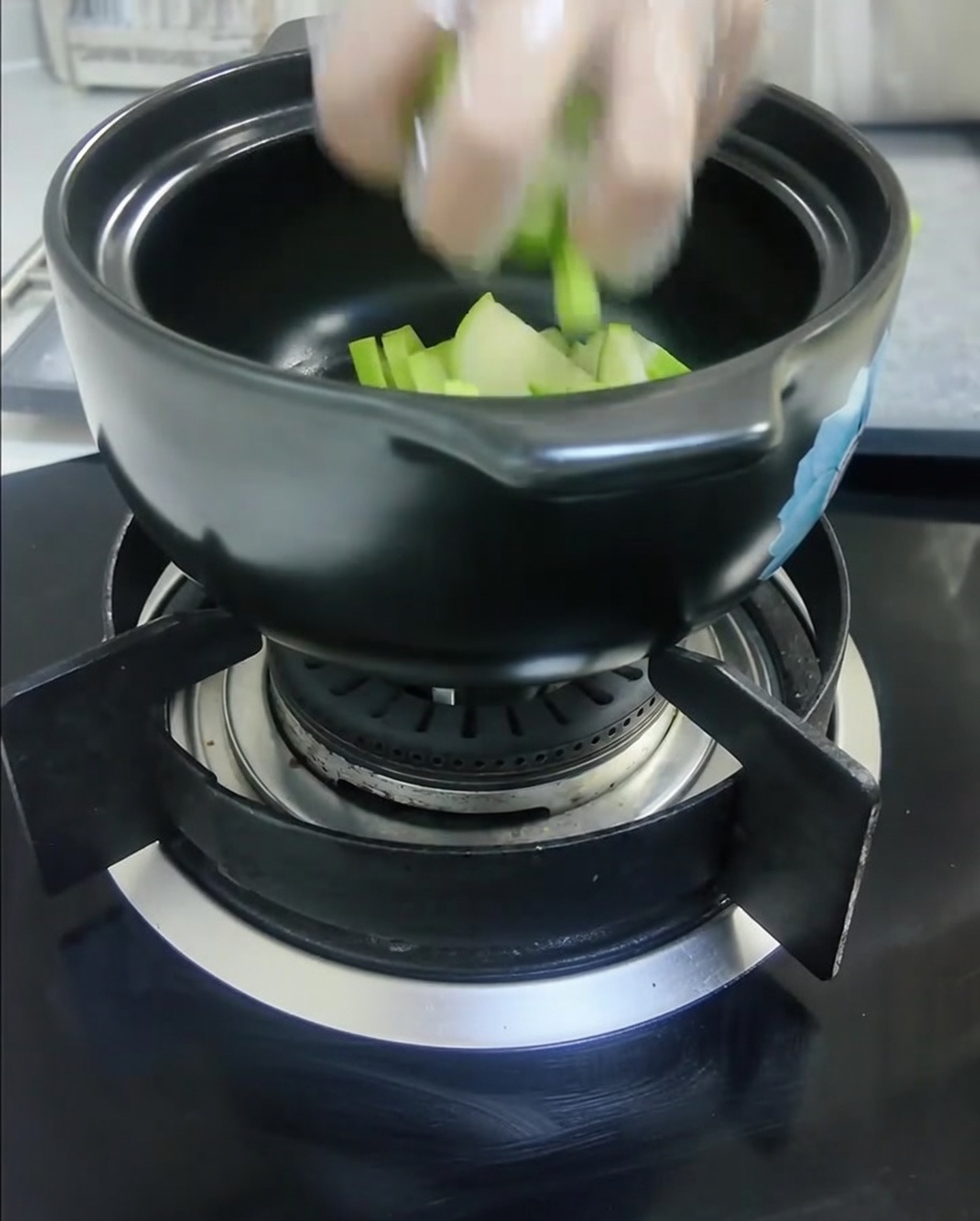 Dés de courge verte et tranches doignon blanc placés dans une marmite en céramique noire.