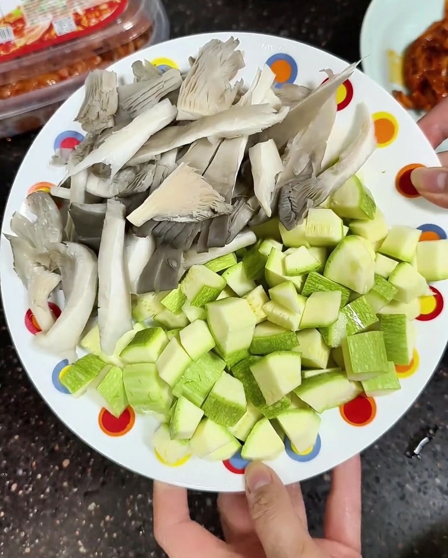 Une assiette contenant des pleurotes émincés et des courgettes en dés prêtes à être cuisinées.