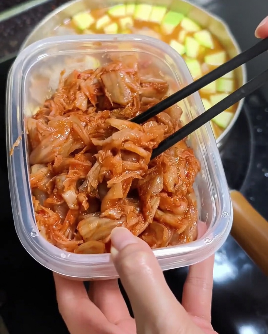 Des baguettes soulevant du kimchi rouge haché au-dessus dune marmite de ragoût chaud.