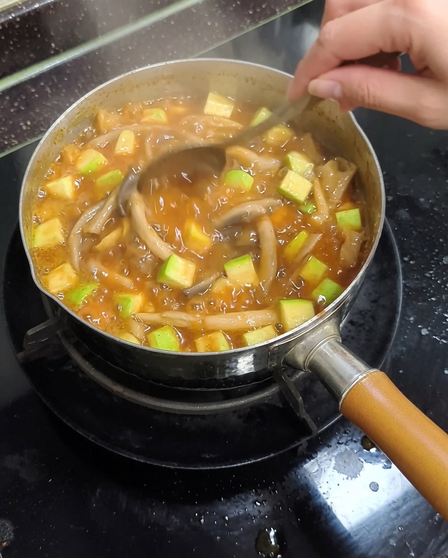 Une marmite en métal sur la cuisinière avec le ragoût en train de bouillir et dêtre mélangé avec une cuillère.