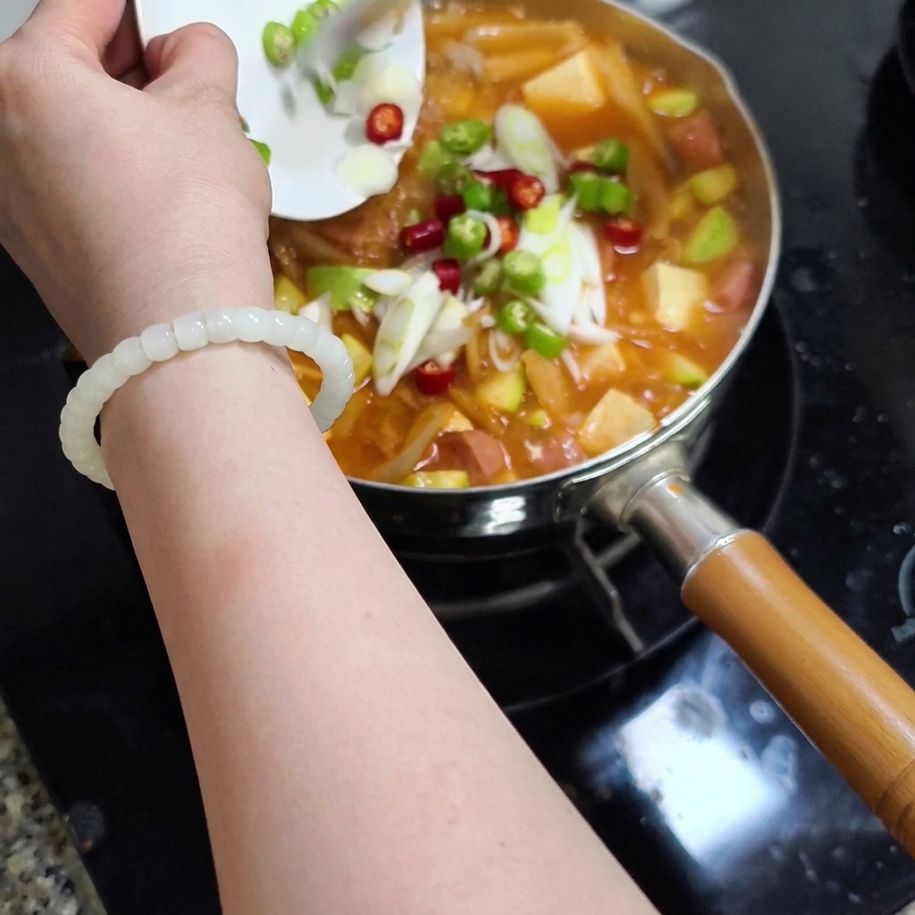 Une main tenant une petite assiette pour verser les piments et ciboules ciselées dans le ragoût.