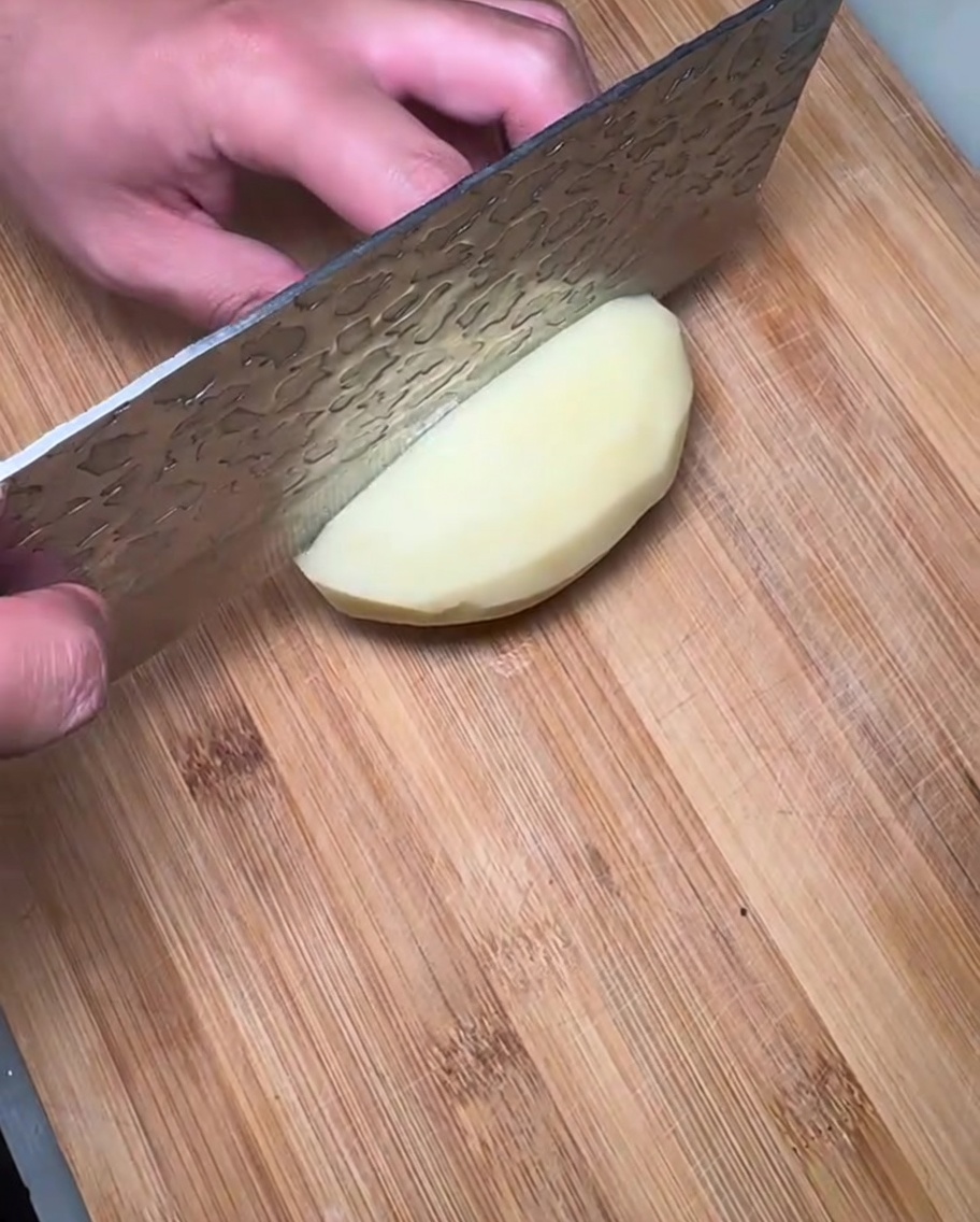 Tranches de pomme de terre crue disposées sur une planche à découper en bois.