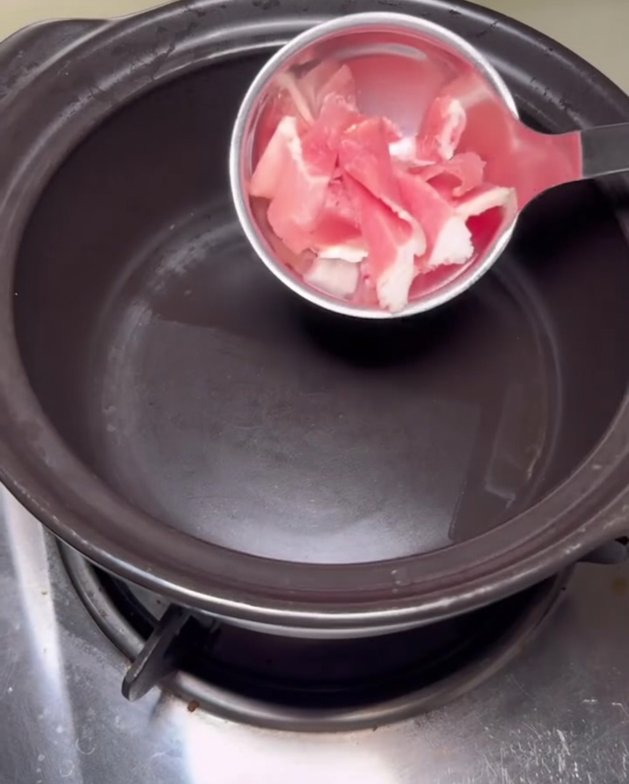 Tranches de poitrine de porc saisies dans un pot en pierre chaude.