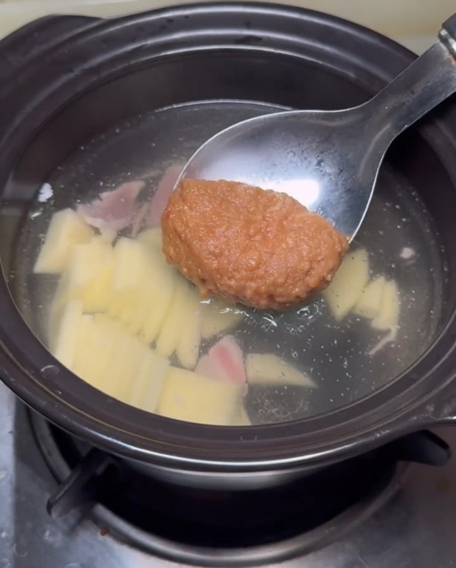 Une louche déposant de la pâte de soja dans le bouillon.