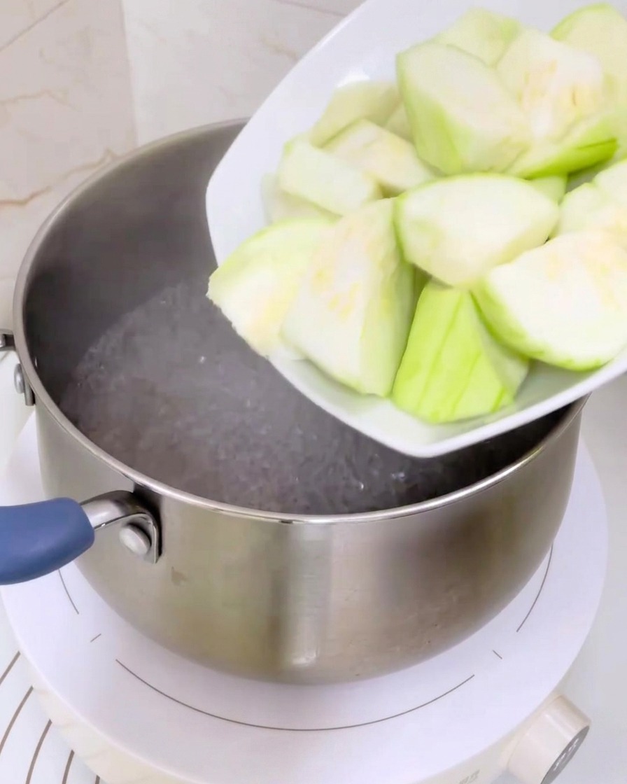 Tranches de luffa vert versées dune assiette blanche dans une casserole deau bouillante.