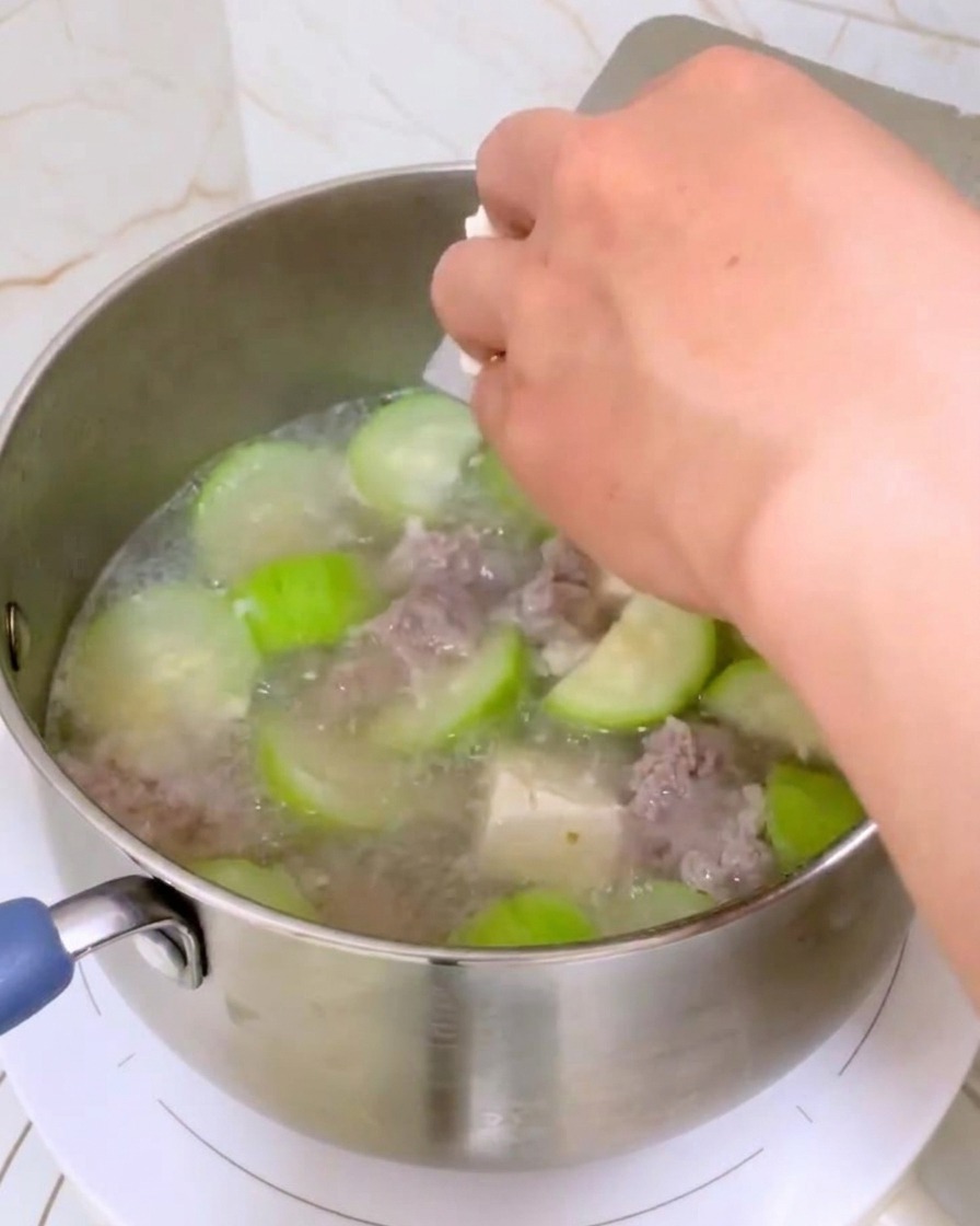 Main déposant des cubes de tofu blanc dans la casserole de soupe.