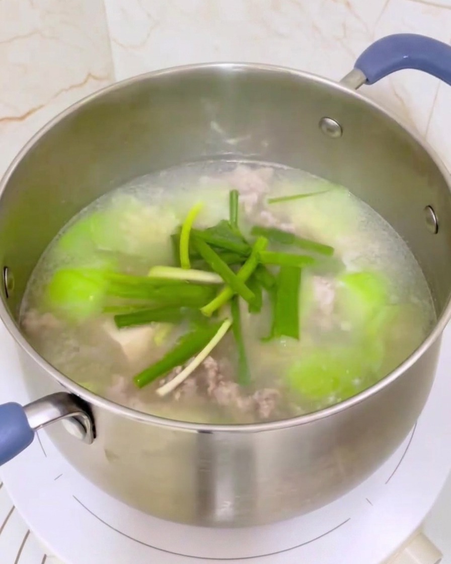Une casserole de soupe au luffa, tofu et viande hachée assaisonnée avec des oignons verts et remuée avec une louche.