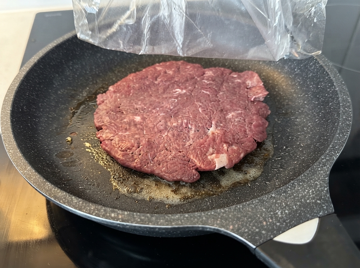 Un grand steak de bœuf cru cuisant dans une poêle antiadhésive graissée sur une cuisinière.