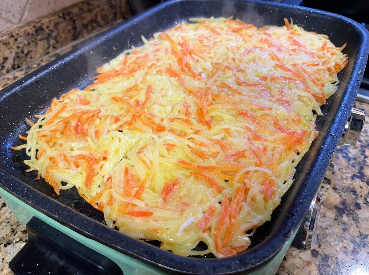 Une grande galette de pommes de terre découpée en plus petites portions à laide de spatules dans une poêle.