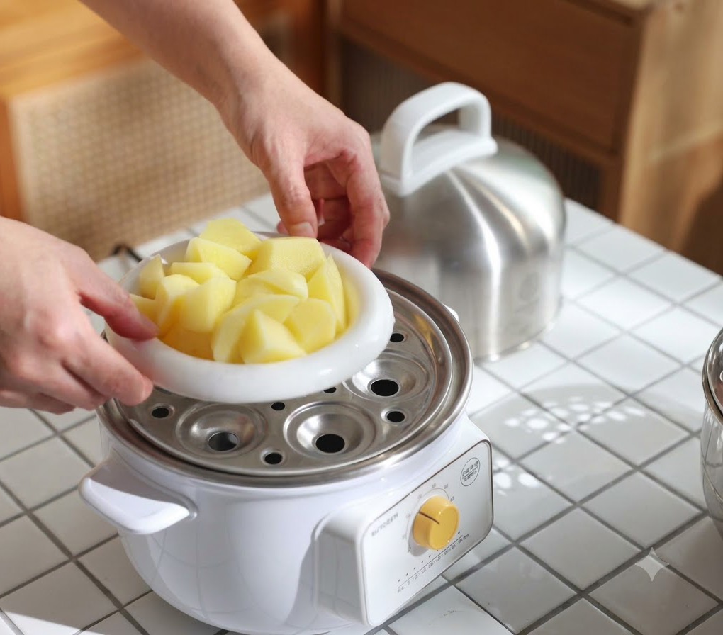 Un plat blanc rempli de morceaux de pommes de terre placé dans un cuiseur vapeur pour les cuire jusquà ce quelles soient tendres.