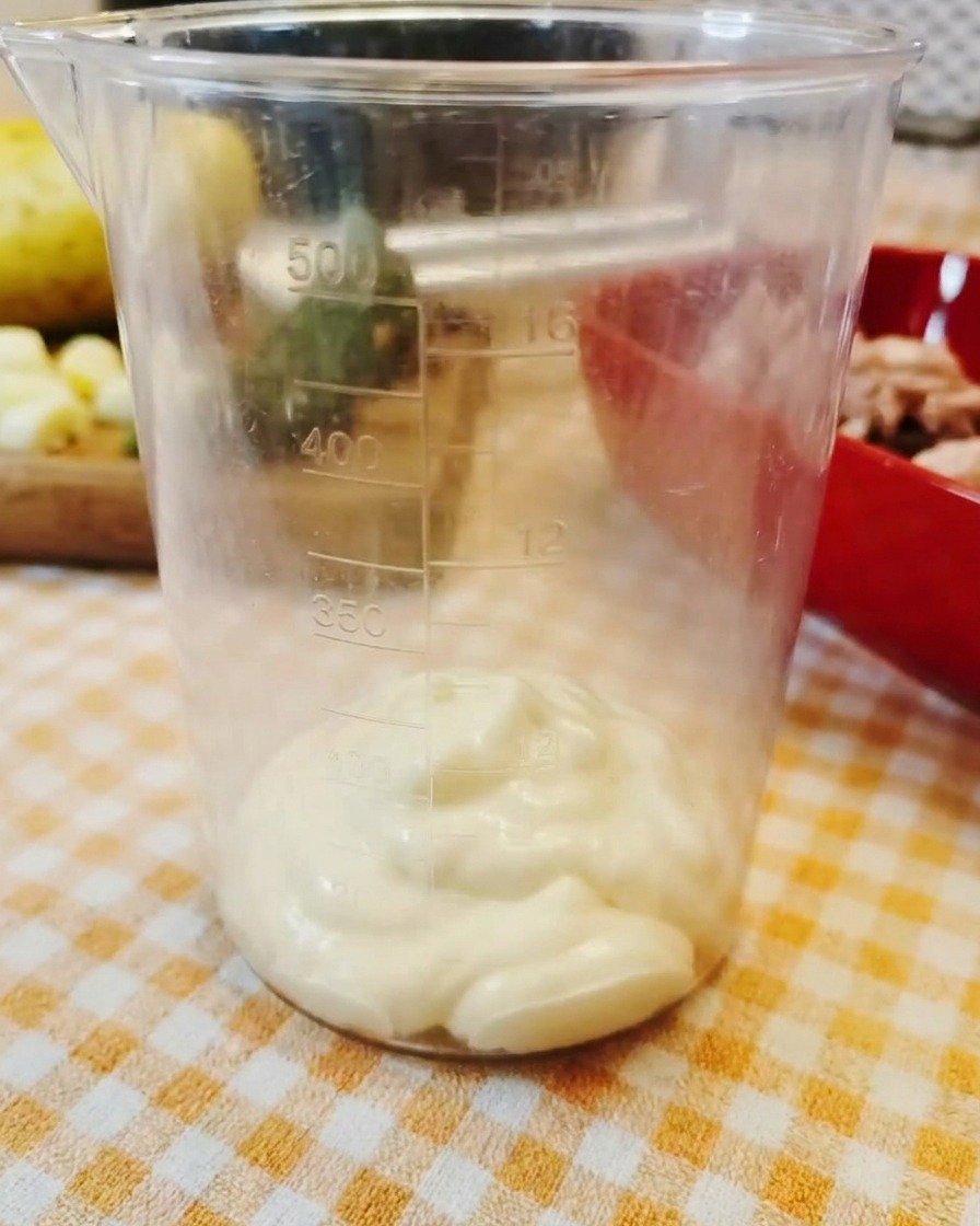 Une cuillerée de mayonnaise épaisse au fond dun verre doseur transparent en plastique.