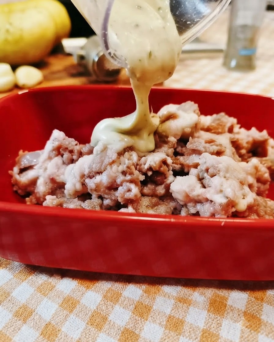 La sauce est versée depuis un récipient transparent dans un bol rouge rempli de bœuf haché.