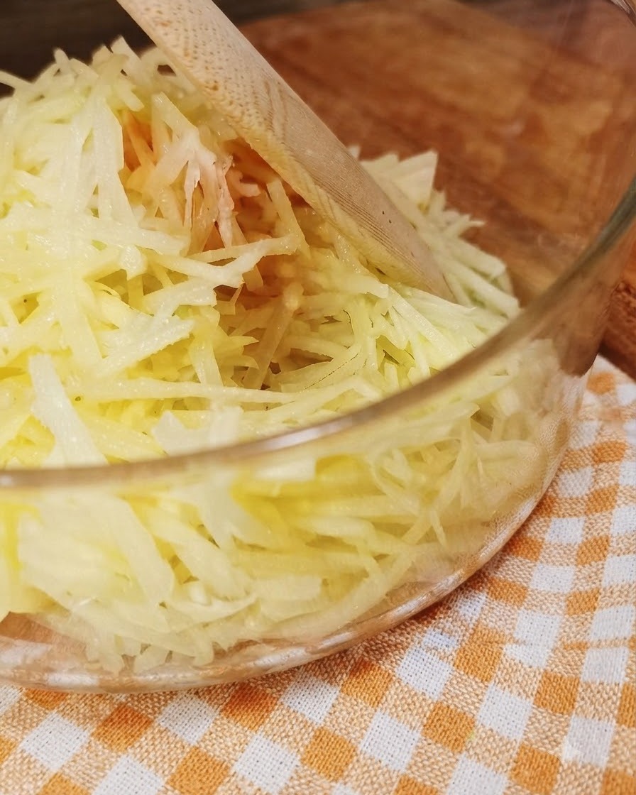 Pommes de terre fraîchement râpées dans un bol en verre transparent avec un ustensile en bois.