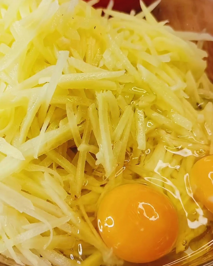 Des œufs entiers cassés directement sur un bol de pommes de terre crues râpées et dassaisonnements.