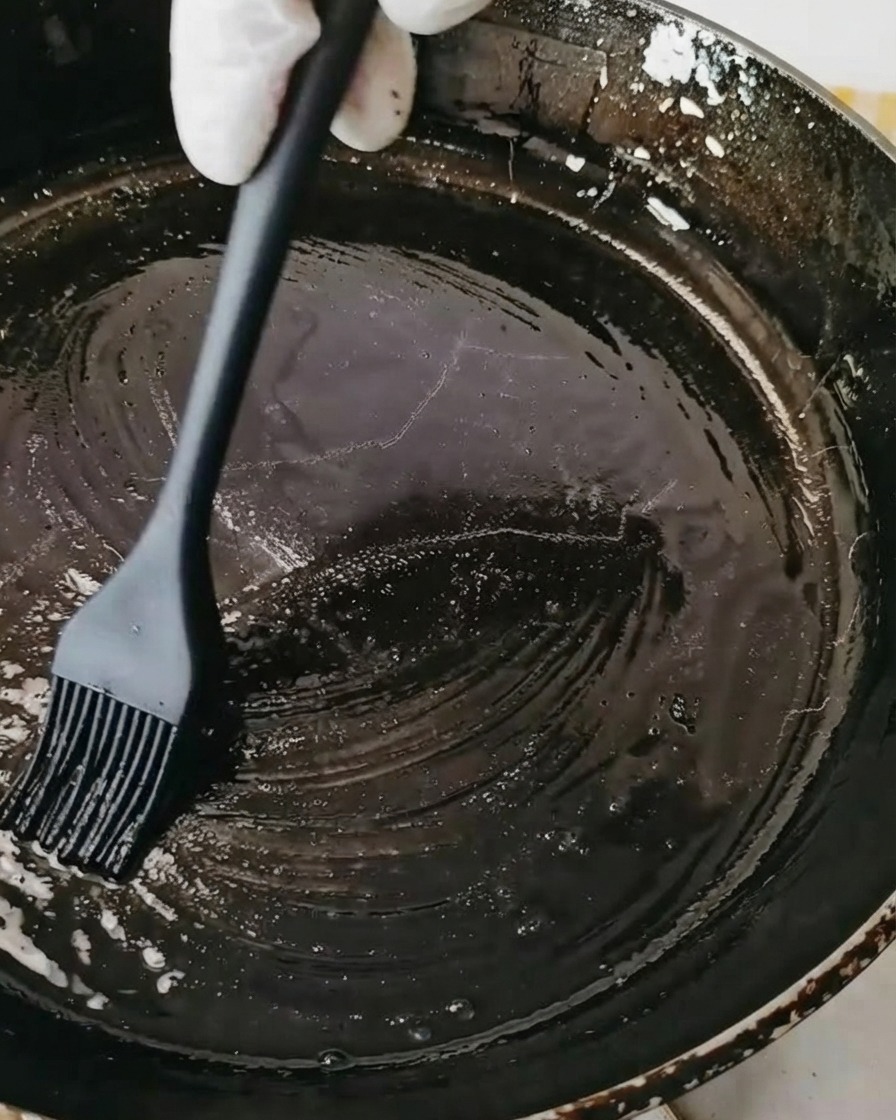 Une poêle noire badigeonnée dhuile à laide dun pinceau en silicone noir.