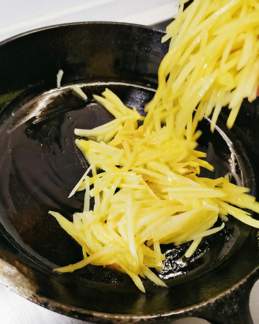 Les pommes de terre râpées sont versées et étalées dans la poêle noire huilée.