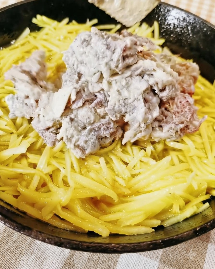 Du bœuf haché assaisonné déposé sur une couche jaune de pommes de terre râpées dans une poêle.