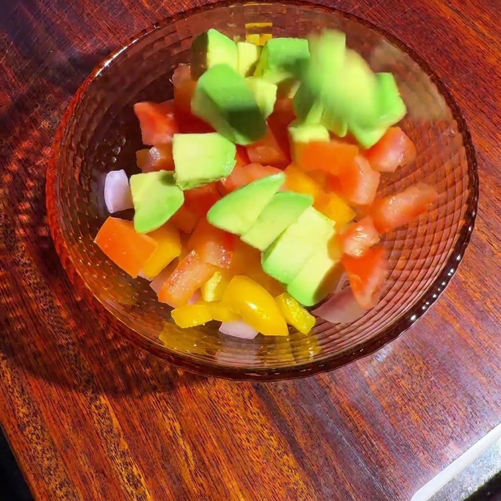 Légumes en dés et avocat dans un bol en verre mélangés avec la vinaigrette.