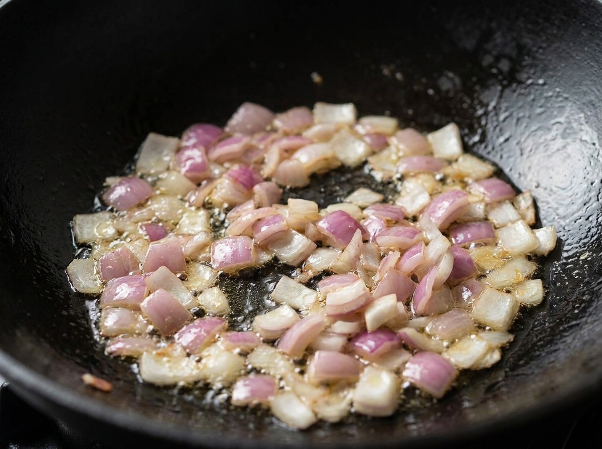Des dés doignons rouges et de bacon en train de grésiller dans de lhuile à lintérieur dun wok noir.
