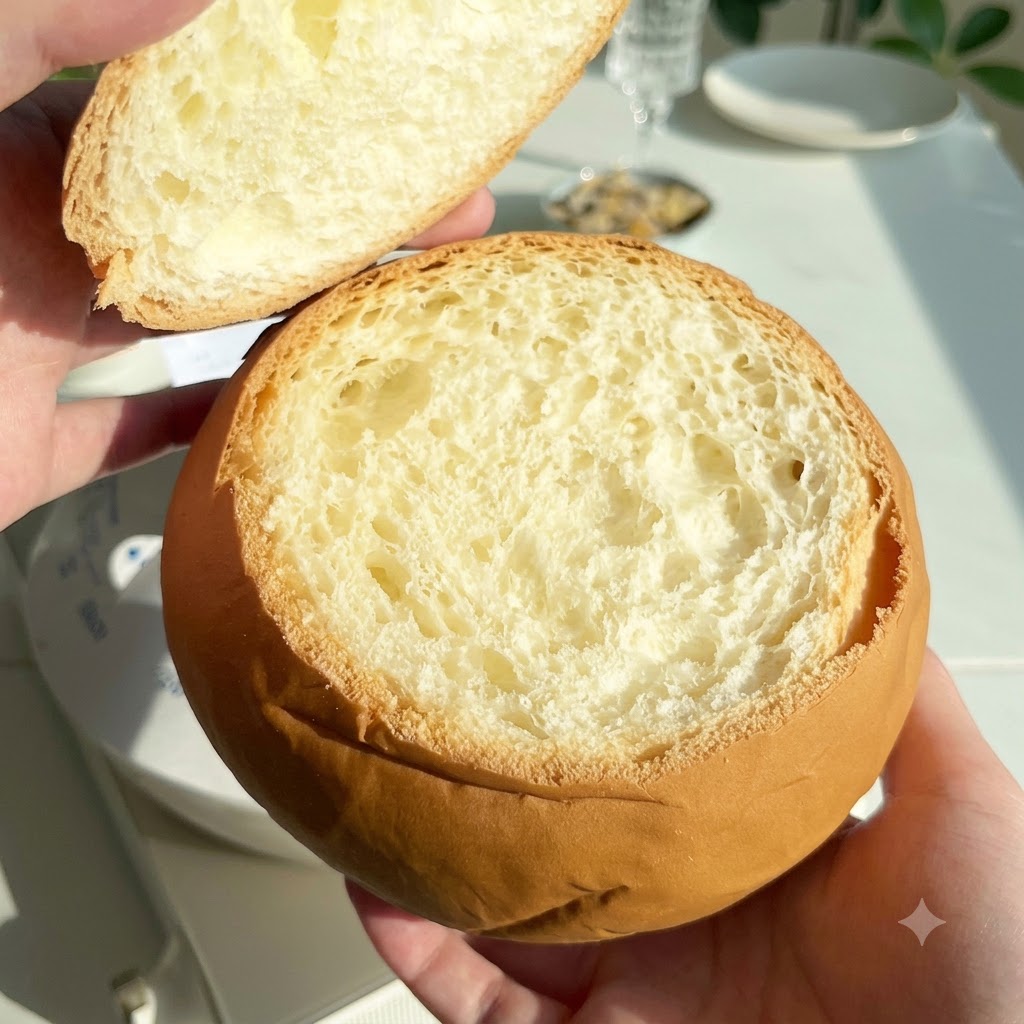 Une miche de pain ronde et creusée tenue avec son couvercle retiré à côté.