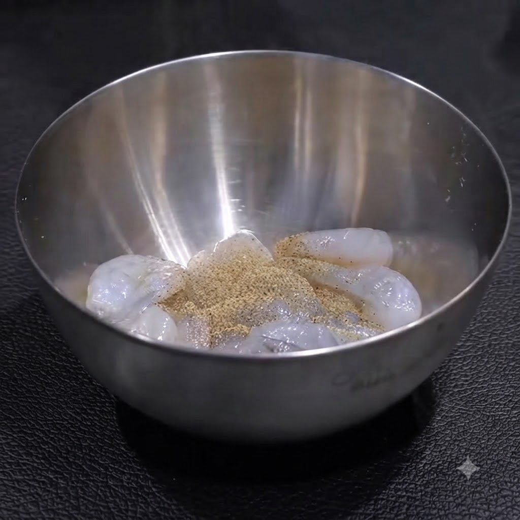 Des crevettes crues dans un bol en acier inoxydable assaisonnées dune couche de poivre et de sel, prêtes à être mélangées.