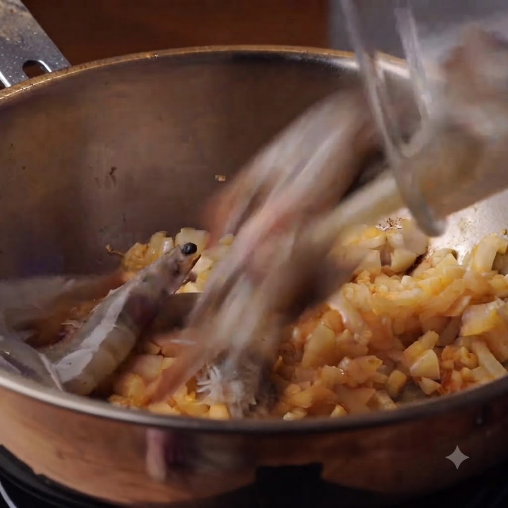 Des crevettes entières fraîches versées dans une casserole contenant des oignons et de lail sautés.