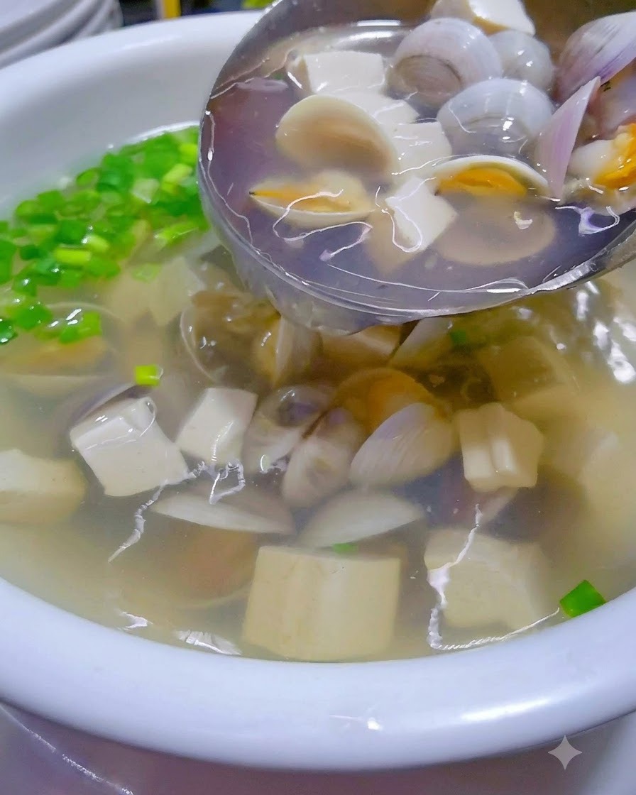 De la soupe chaude aux palourdes et au tofu versée dun wok dans un bol de service garni.
