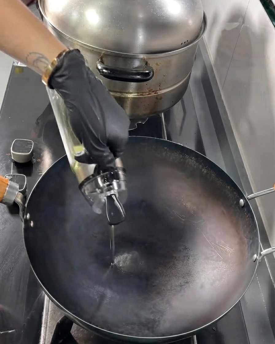 Huile de cuisson versée dune bouteille en verre dans un wok noir chaud.
