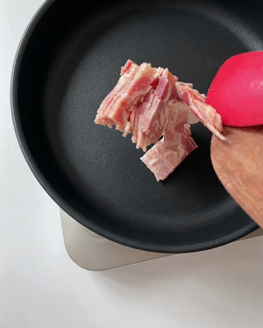 Des morceaux de bacon hachés transférés dune spatule en bois vers une poêle noire chaude.