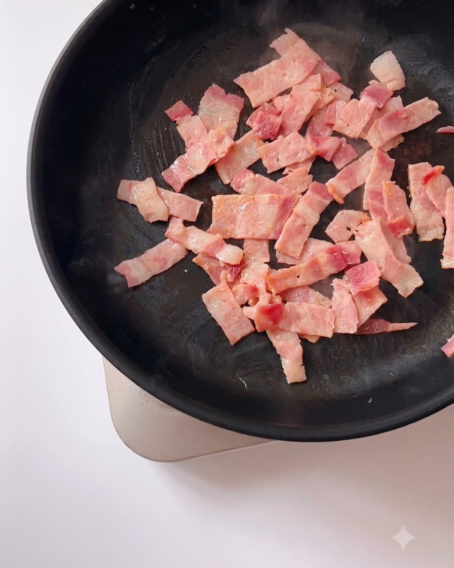 Des jaunes dœufs salés écrasés mélangés à des morceaux de bacon dorés qui grésillent dans une poêle.