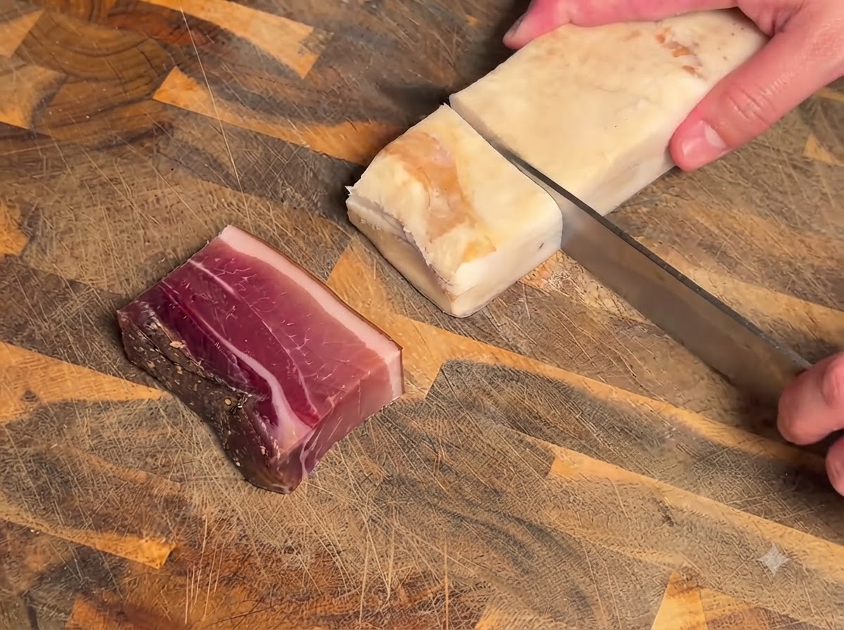 Un couteau coupant un bloc de viande séchée et de bacon sur une planche à découper en bois texturée.