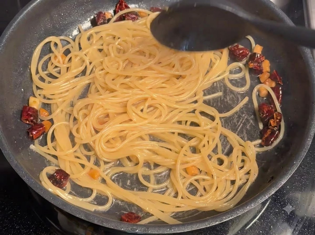 De leau de cuisson des pâtes incorporée en remuant aux spaghettis et au porc dans une poêle.