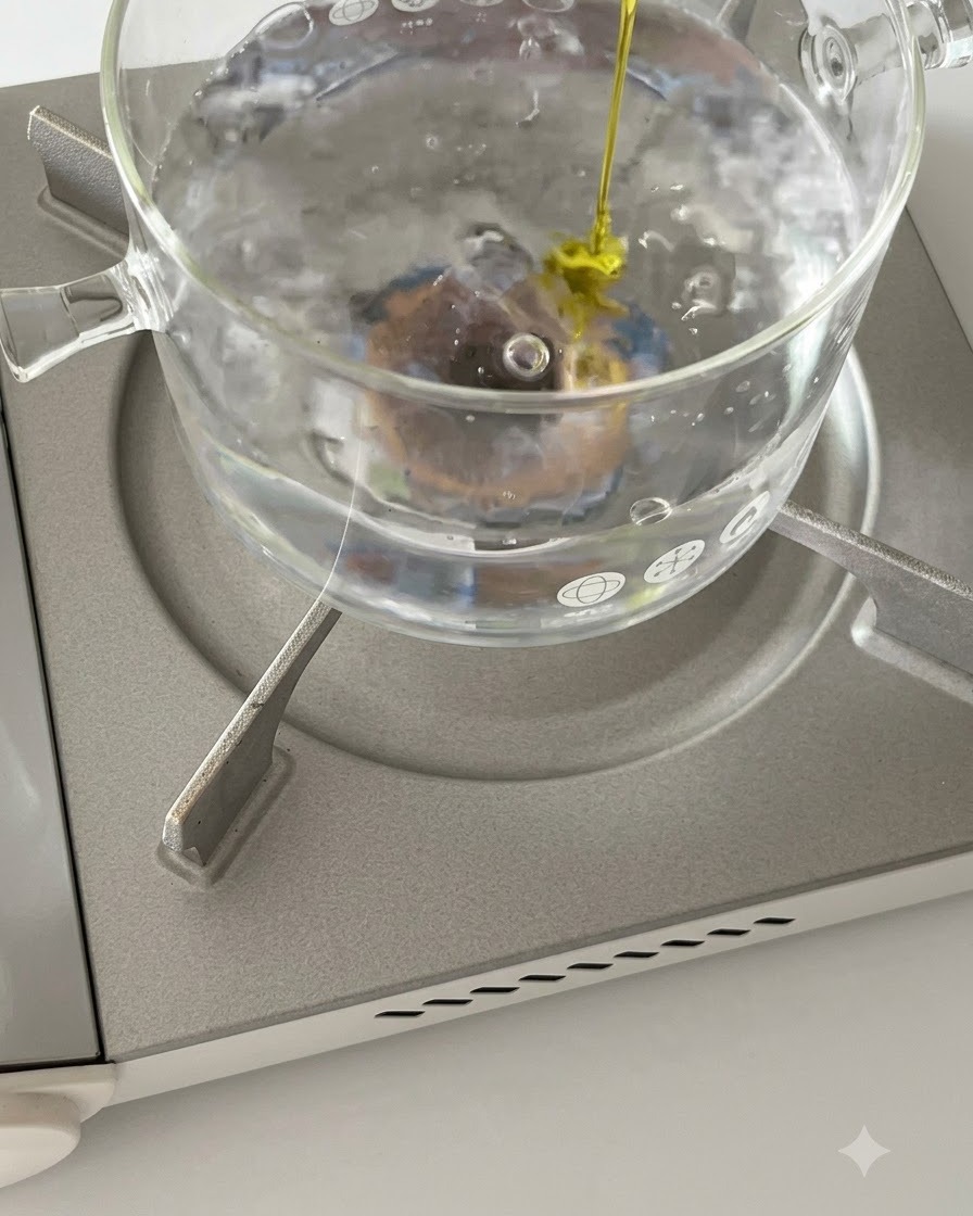 Des rigatoni qui bouillissent dans une casserole en verre sur une cuisinière avec un filet dhuile dolive versé dedans.