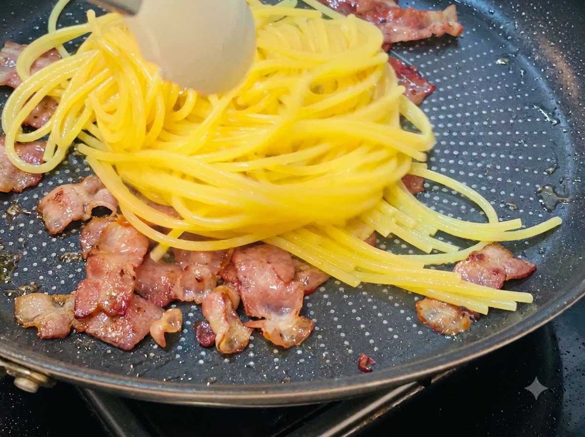 Spaghettis cuits soulevés et transférés dans une poêle contenant les morceaux de bacon croustillants.