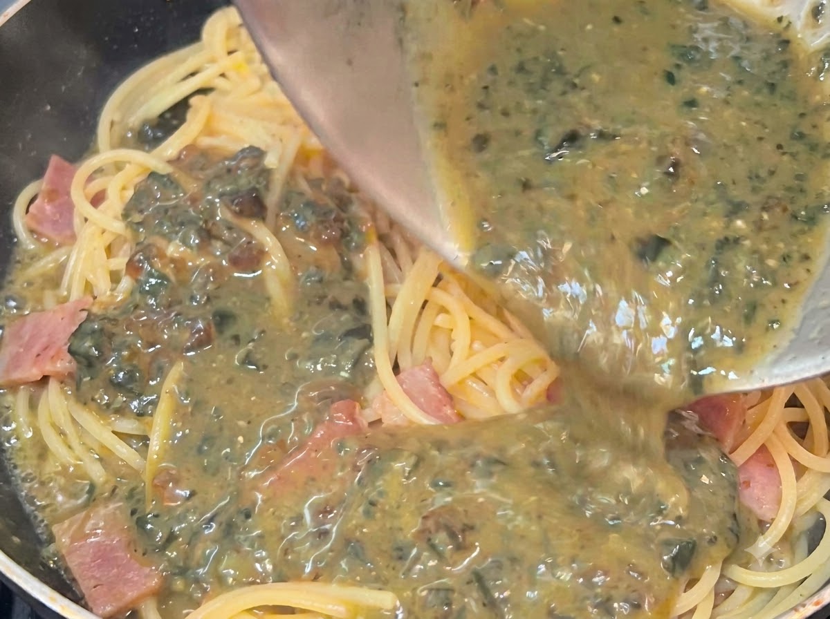 Sauce crémeuse aux œufs préservés versée dun bol sur les spaghettis chauds et le bacon dans une poêle.