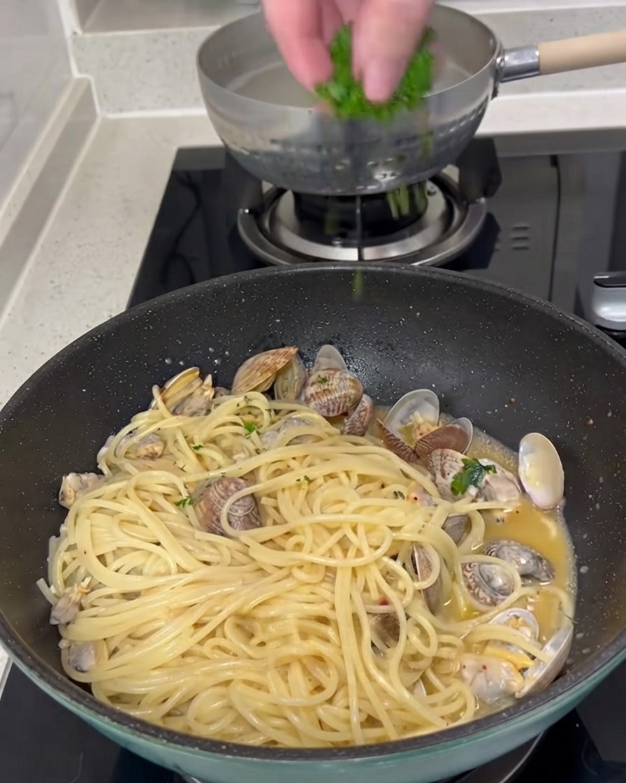 Du persil vert frais haché saupoudré par-dessus une poêle de spaghetti et de palourdes cuits.