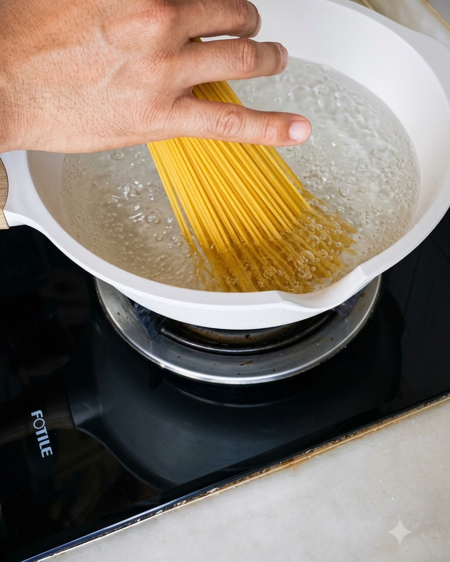 Une poignée de spaghettis secs plongés dans une casserole blanche remplie deau bouillante.