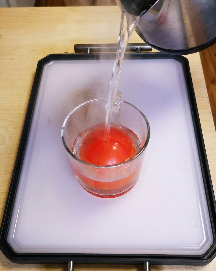 De leau chaude versée dune bouilloire dans un verre contenant une tomate rouge fraîche.