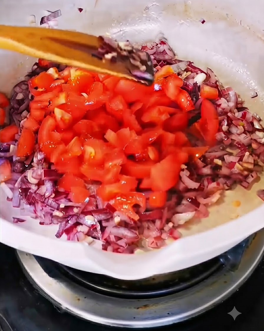 Des tomates fraîches hachées ajoutées dans une poêle contenant les oignons et lail sautés.