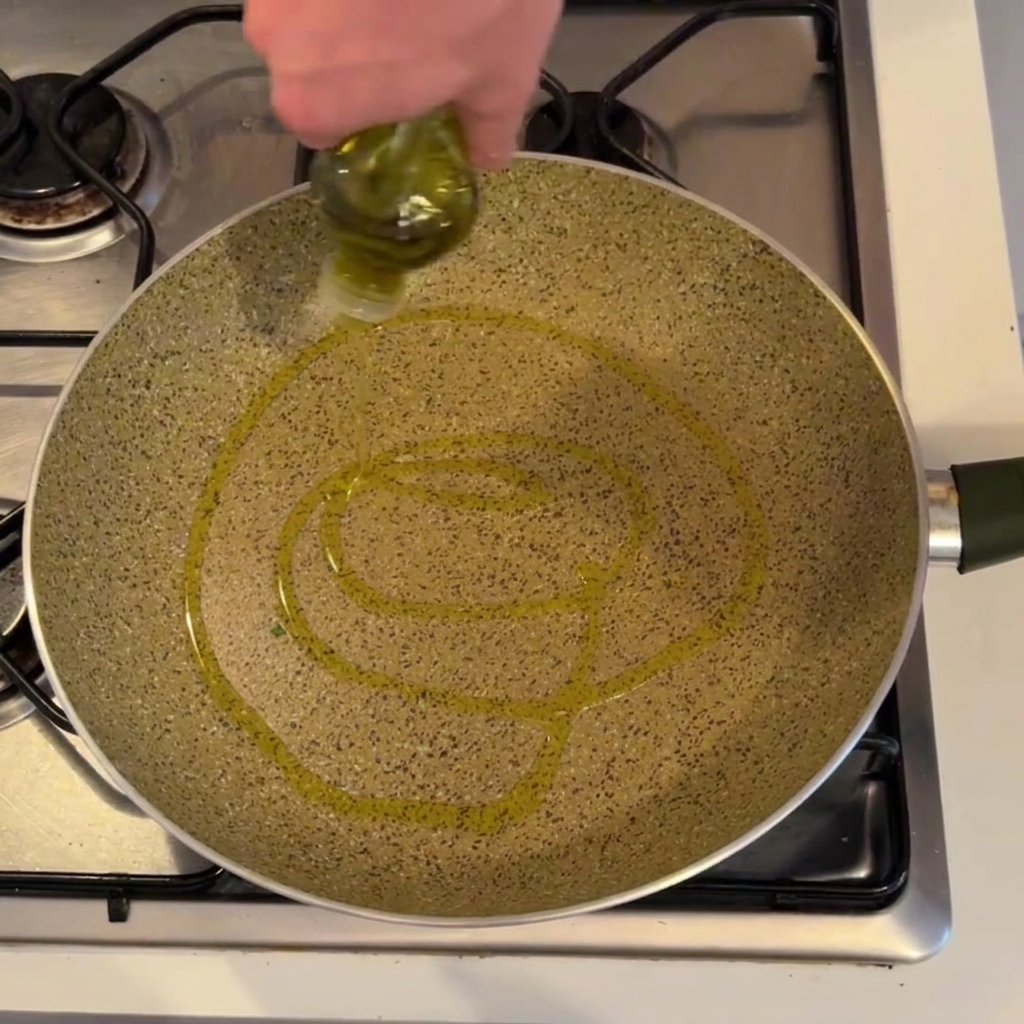 Une personne verse de lhuile dolive dune bouteille dans une grande poêle mouchetée sur une cuisinière à gaz.