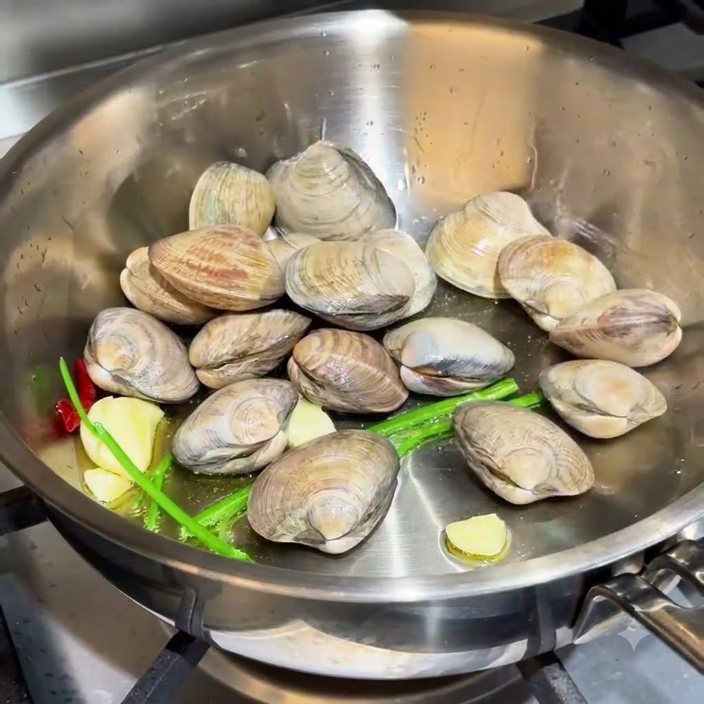 Palourdes éparpillées dans la poêle aux côtés de lail et des racines de ciboulette.