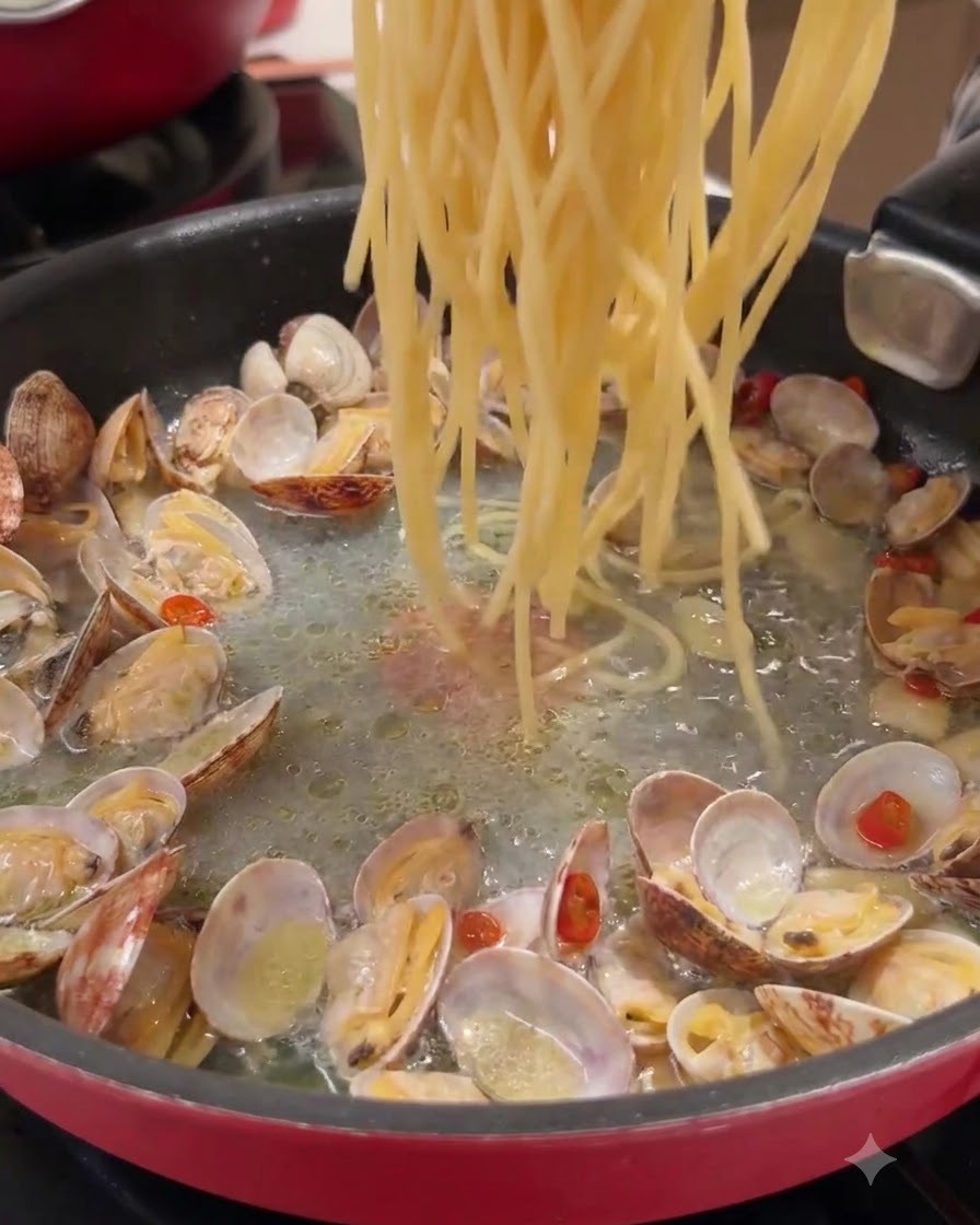 De longs brins de pâtes jetés dans une poêle contenant des palourdes cuites et du jus assaisonné.