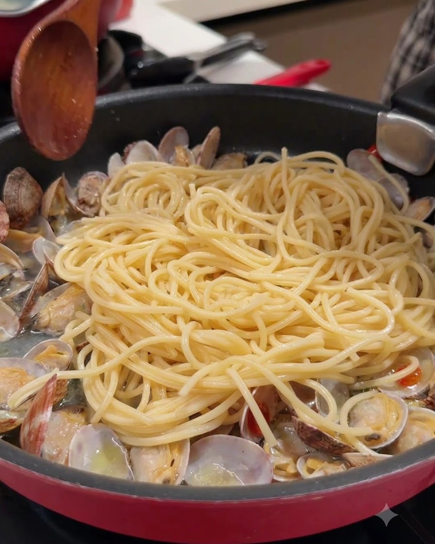 Une cuillère en bois et des spaghettis dans une poêle avec des palourdes ouvertes et du bouillon.