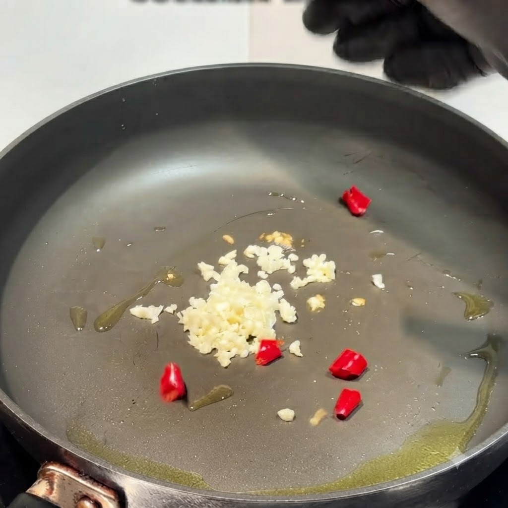 Ail haché et morceaux de piment rouge dispersés dans une poêle huilée.