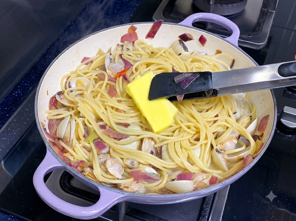 Une noix de beurre jaune fondant dans une poêle de spaghetti et de palourdes mélangés.