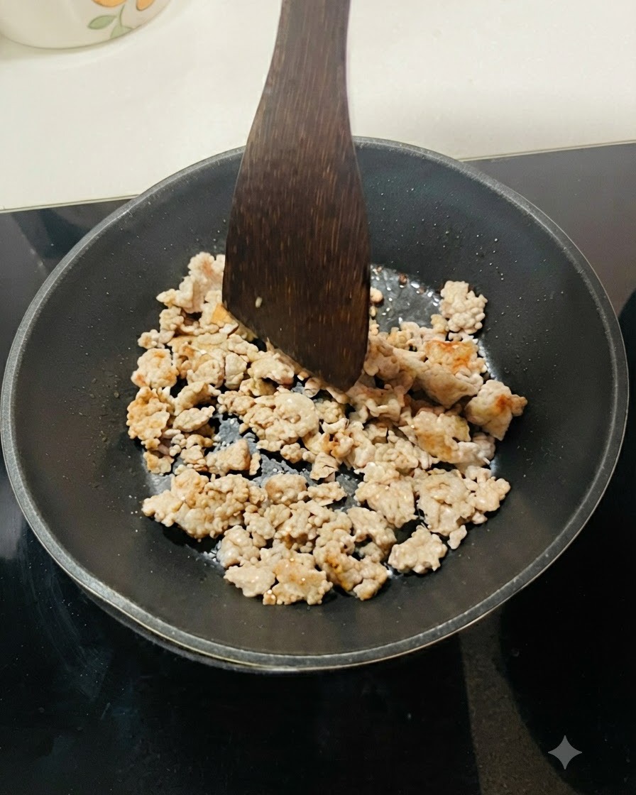 De la viande hachée en train de frire dans une poêle noire, séparée en petits morceaux avec une spatule en bois.