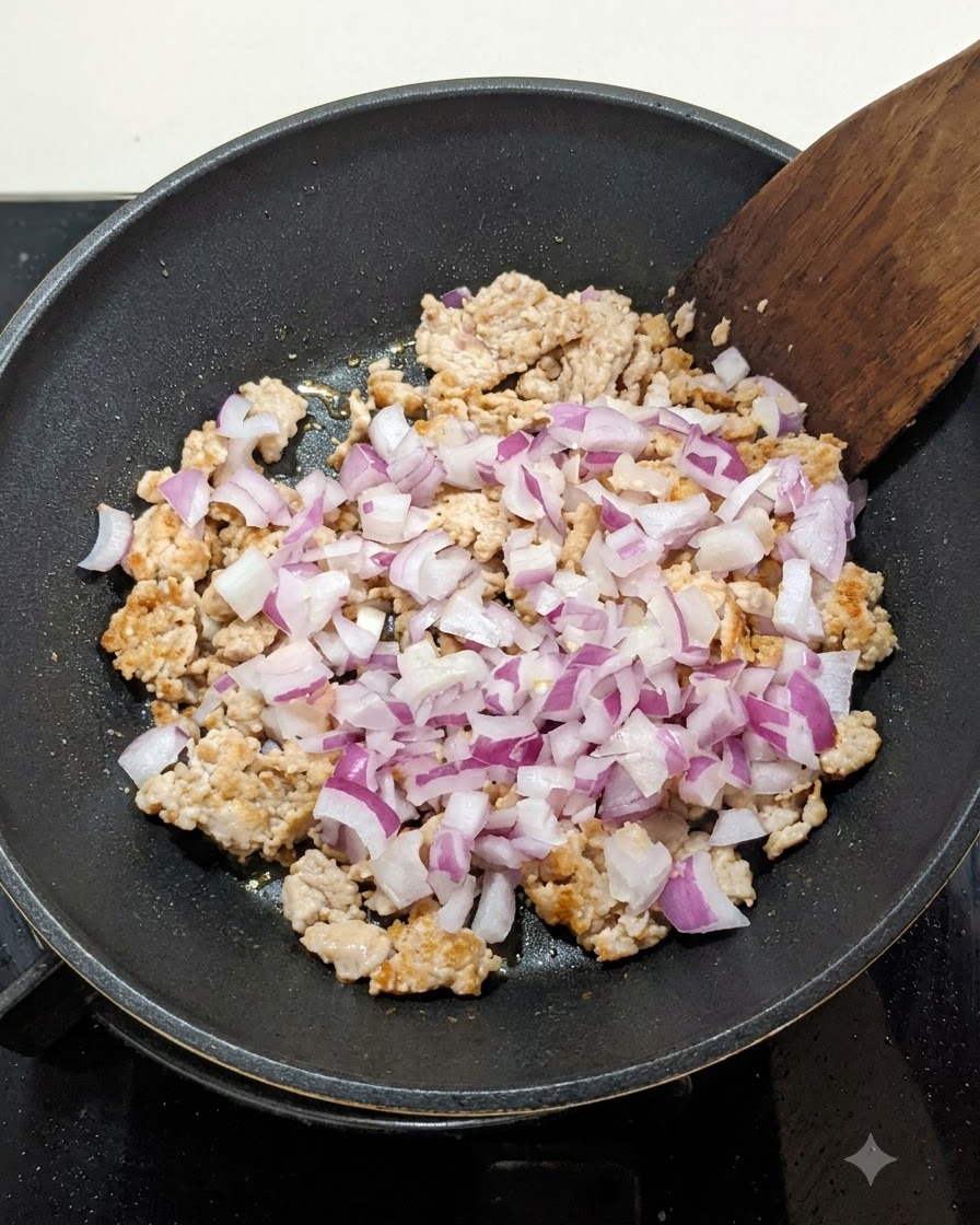 Des oignons rouges en dés mélangés à la viande hachée dorée dans une poêle, remués avec une spatule en bois.