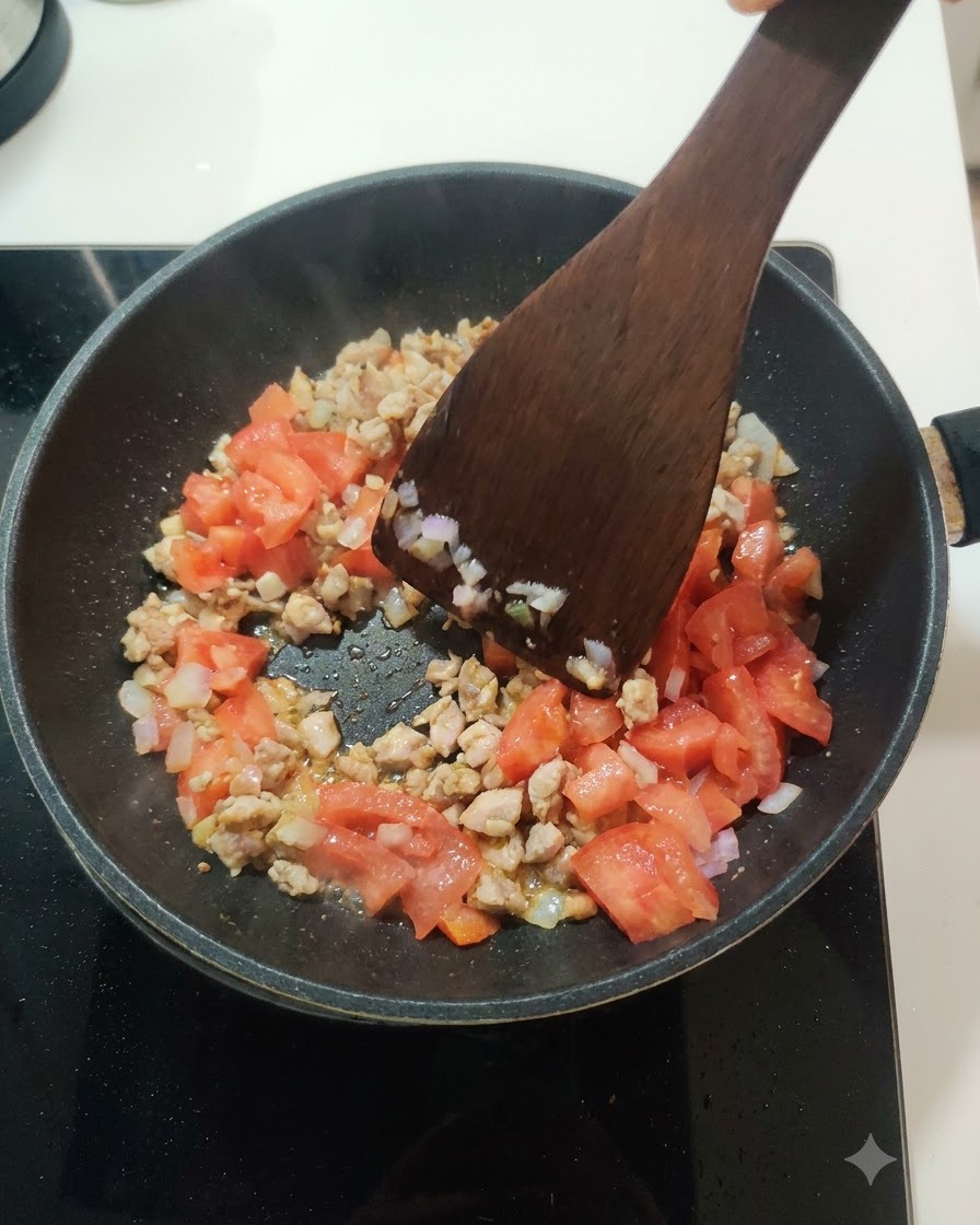 Des tomates fraîches en dés en train dêtre incorporées au mélange de viande et doignons dans une poêle.
