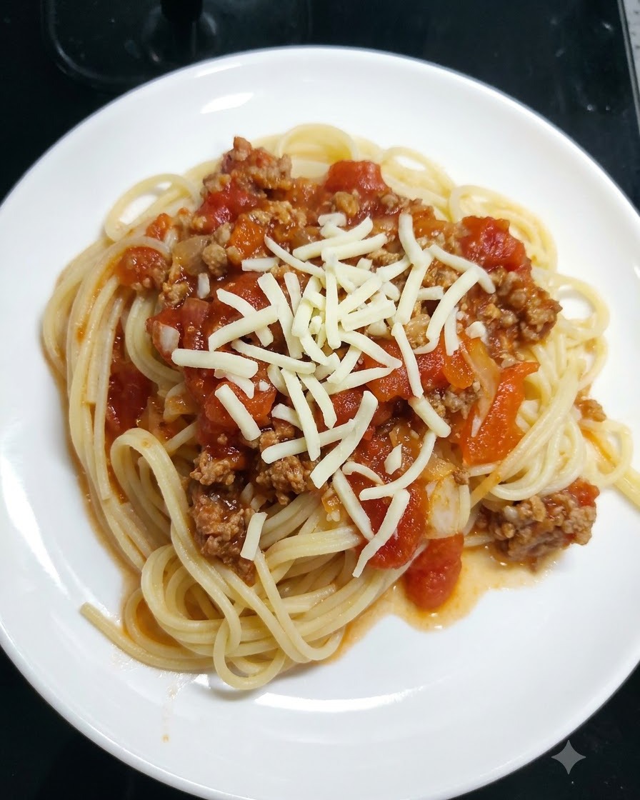 Du fromage mozzarella râpé saupoudré sur des spaghettis recouverts de sauce tomate dans une assiette blanche.