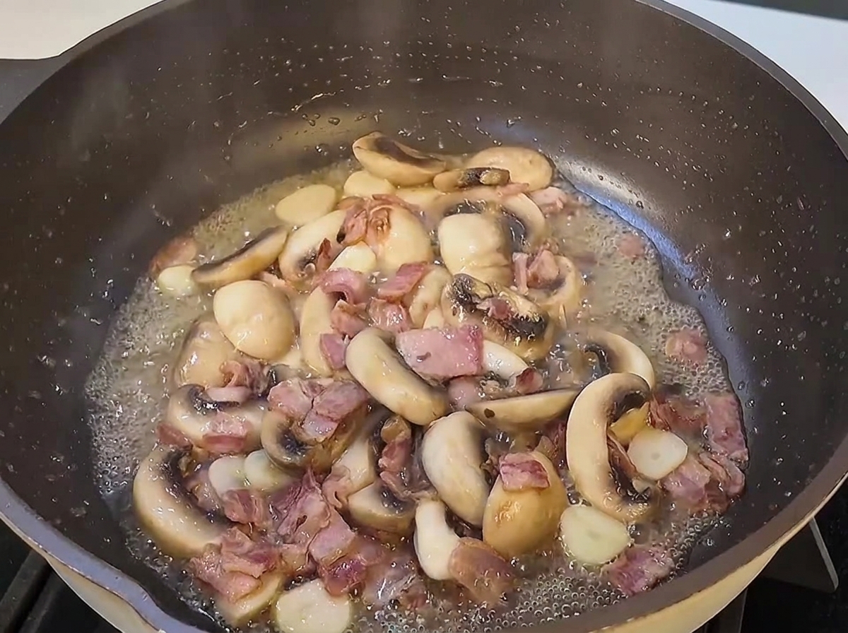 Les spaghettis cuits ajoutés dans la poêle avec les champignons et les lardons dorés.